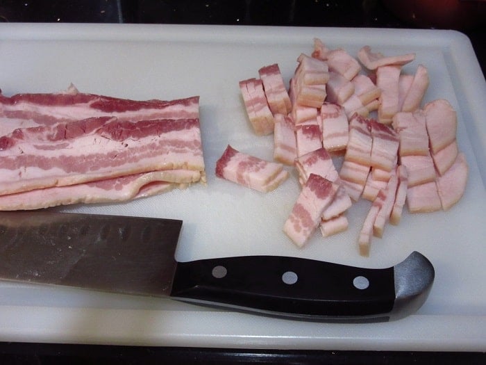Bacon being cut into pieces on a cutting board.