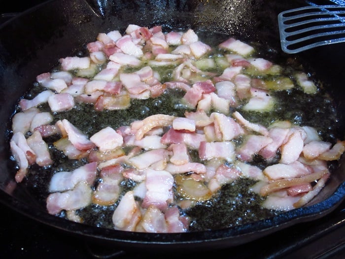Bacon frying in oil in a cast iron skillet.