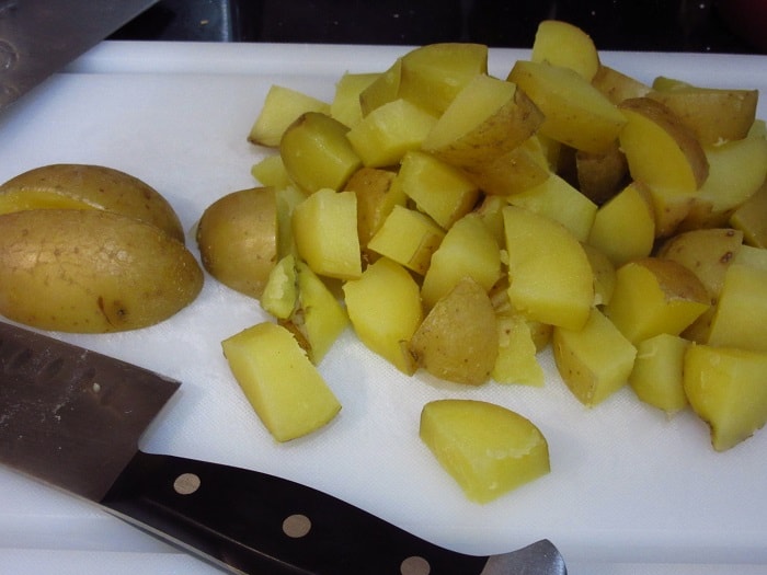 Cooked golden potatoes being cut into bite-sized pieces.