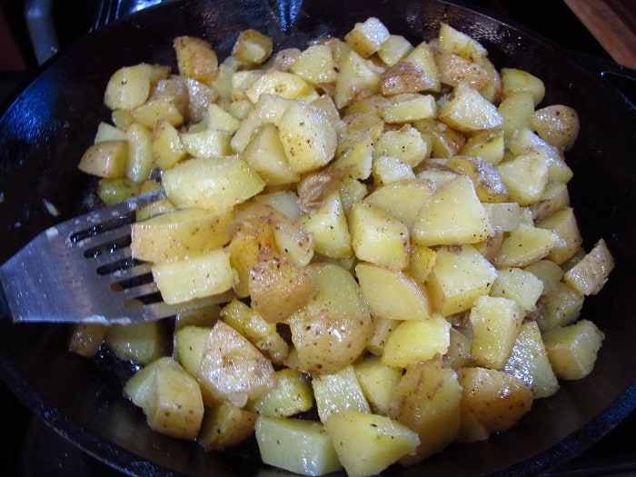 Potatoes in a cast iron skillet with a slotted spatula.