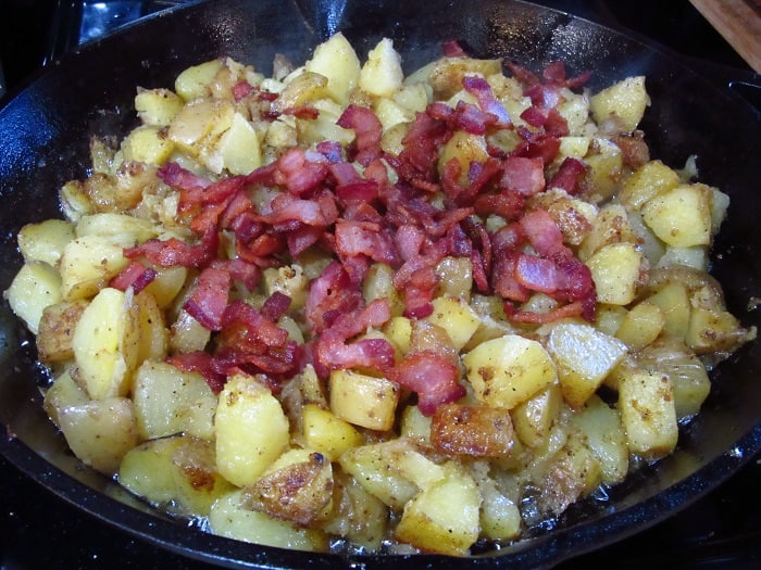 Cooked bacon added to fried potatoes in a cast iron skillet.