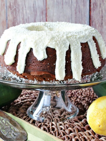 A Gingerbread Bundt Cake wit Zucchini on a cake stand with a lemon and zucchini on the table.