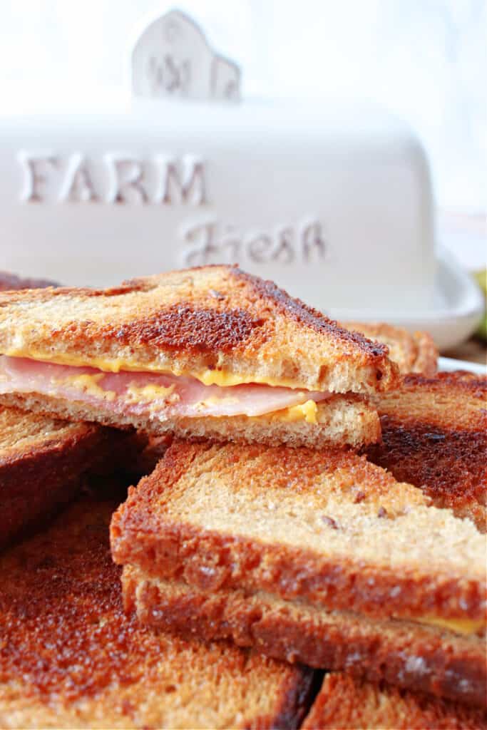 A vertical closeup of a stack of Grilled Ham and Cheese Appetizers along with a cute butter dish in the background.