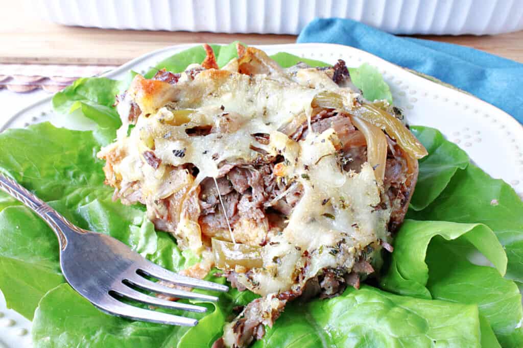 A horizontal closeup of a serving of Italian Beef Bread Pudding on a plate with a fork and some butter lettuce.