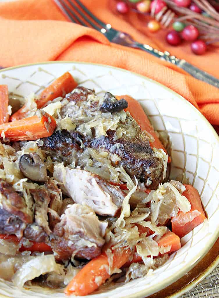 A vertical closeup of German Pork Ribs with Sauerkraut in a bowl with an orange napkin on the side along with a fork.