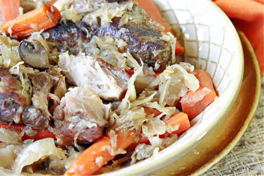 A closeup offset photo of a bowl of German Pork Ribs and Sauerkraut along with mushrooms and carrots.