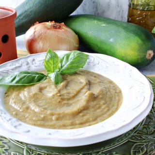 A white bowl filled with Roasted Garlic and Zucchini Soup along with some fresh basil and a spoon on the side.