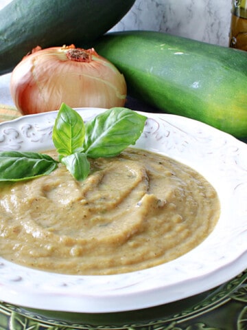A white bowl filled with Roasted Garlic and Zucchini Soup along with some fresh basil and a spoon on the side.