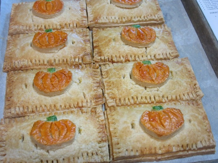 A horizontal photo of eight Pumpkin Hand Pies on a baking sheet with painted pie crust embellished pumpkins on top.