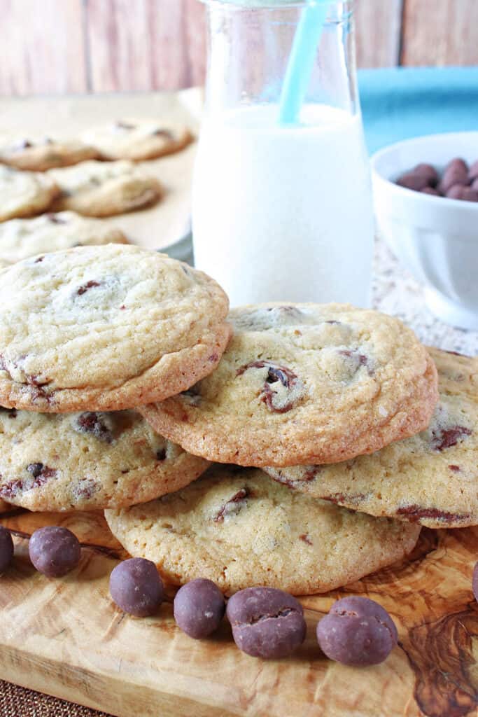 A vertical closeup of a stack of Chocolate Chip Espresso Bean Cookies with a glass of milk with a blue straw in the background.