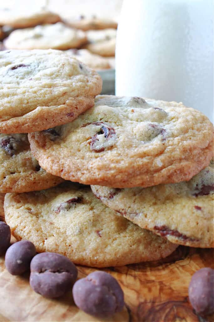 A vertical closeup of some Chocolate Chip Espresso Bean Cookies on a wooden board along with chocolate covered espresso beans.