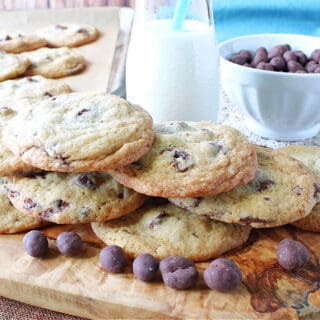 A photo of a stack of Chocolate Chip Espresso Cookies on a wooden board with a glass of milk and a blow of chocolate chips in the background.