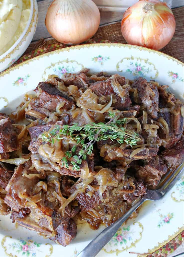 A vertical closeup of a platter of French Onion Short Ribs with caramelized onions and fresh thyme on top.