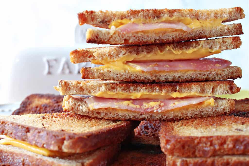 A closeup of a stack of cut Grilled Ham and Cheese Appetizers on mini cocktail bread with melted cheese and ham inside.