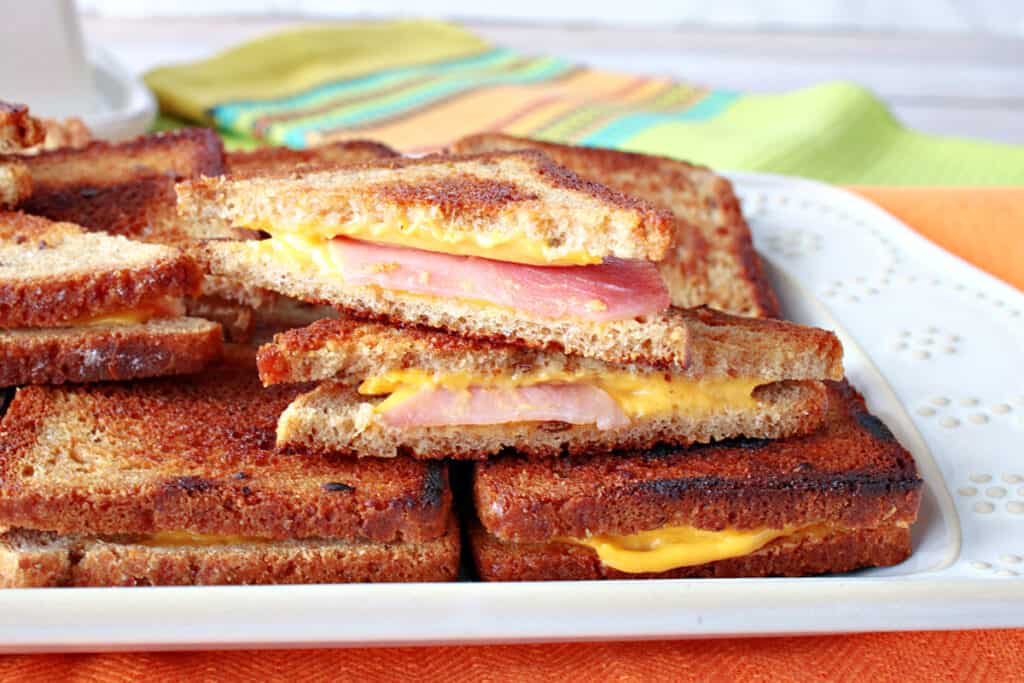 A horizontal close up of a platter of mini Grilled Ham and Cheese Appetizer sandwiches with melted cheese and ham.