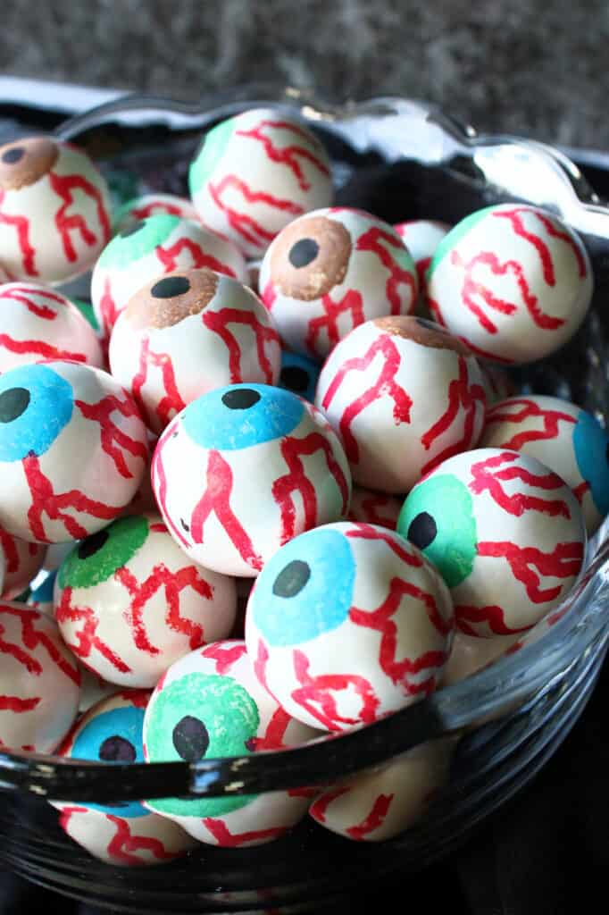 A vertical closeup of blue, green, and brown Gumball Eyeballs in a glass bowl with red eye veins.