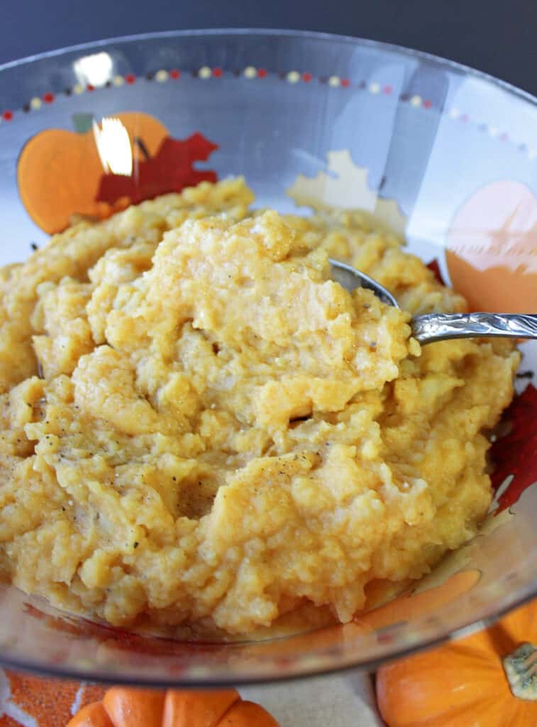 A vertical closeup of a bowl filled with Pumpkin Mashed Potatoes along with a serving spoon.