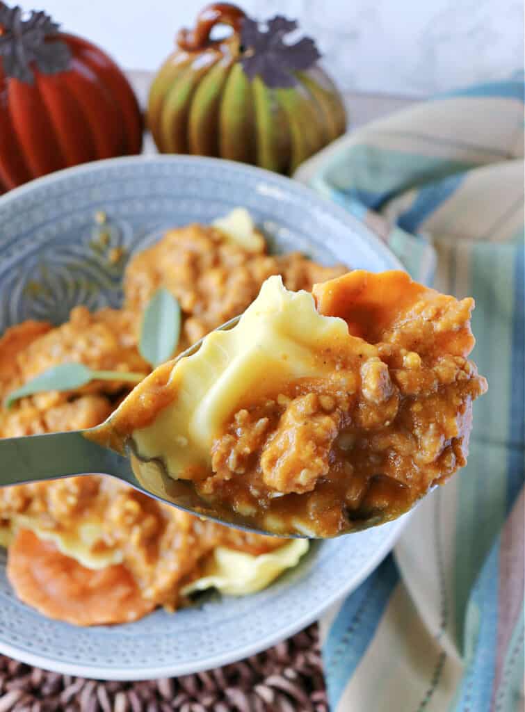 A vertical closeup of a serving spoon holding some Ravioli with Pumpkin Vodka Sauce.