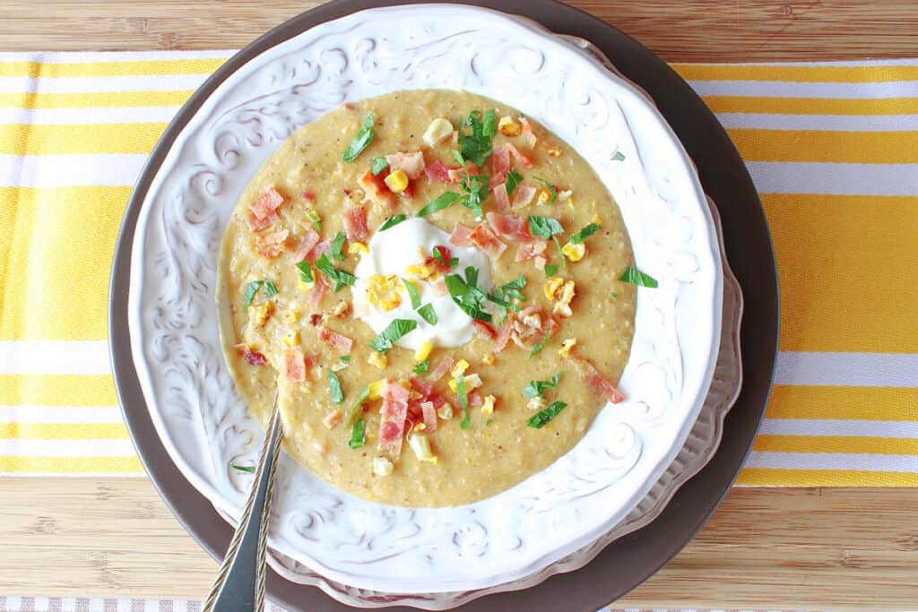 A direct overhead photo of a bowl of Roasted Corn and Potato Chowder with a yellow and white striped napkin underneath.