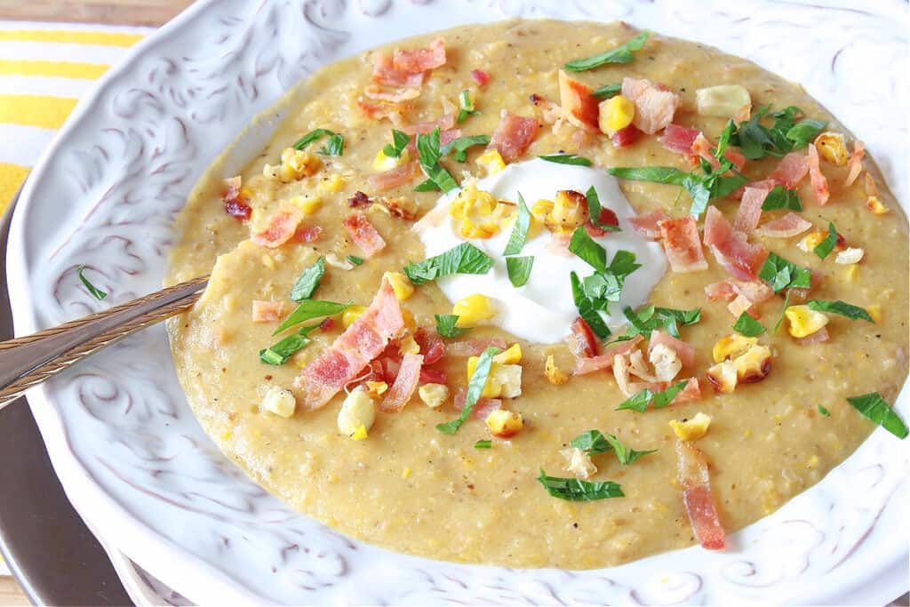 A closeup offset horizontal photo of a bowlful of Roasted Corn and Potato Chowder with a dollop of sour cream and a spoon.