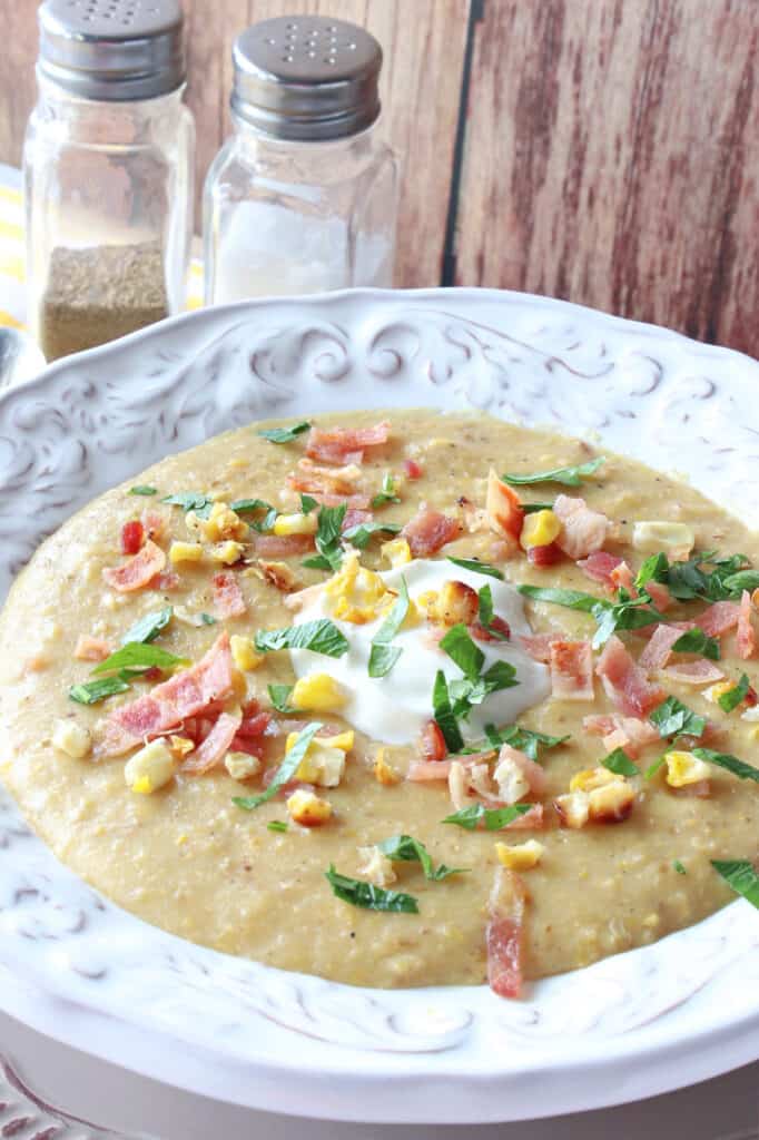 A vertical closeup of a bowl filled with Roasted Corn and Potato Chowder along with a garnish of corn kernels, bacon, and chopped parsley.