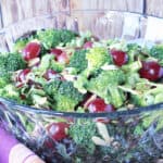 A glass bowl filled with Sweet and Sour Broccoli Salad with fresh broccoli, red grapes, and slivered almonds.