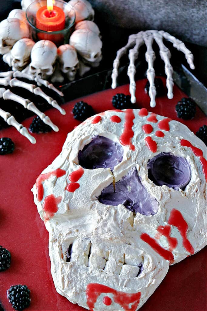 A vertical overhead closeup of a Swiss Meringue Skull with strawberry jelly blood and marshmallow teeth.