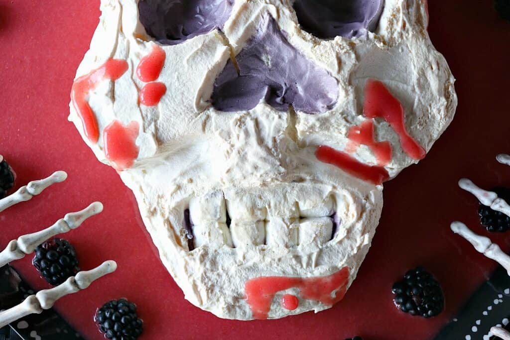 An overhead closeup photo of the mouth of a Swiss Meringue Skull with mini-marshmallow teeth and  strawberry jelly blood.