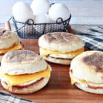 Four Copycat Egg McMuffin Sandwiches on a board with eggs in the background.