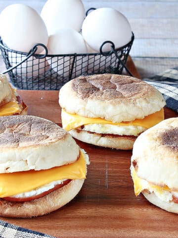 Four Copycat Egg McMuffin Sandwiches on a board with eggs in the background.