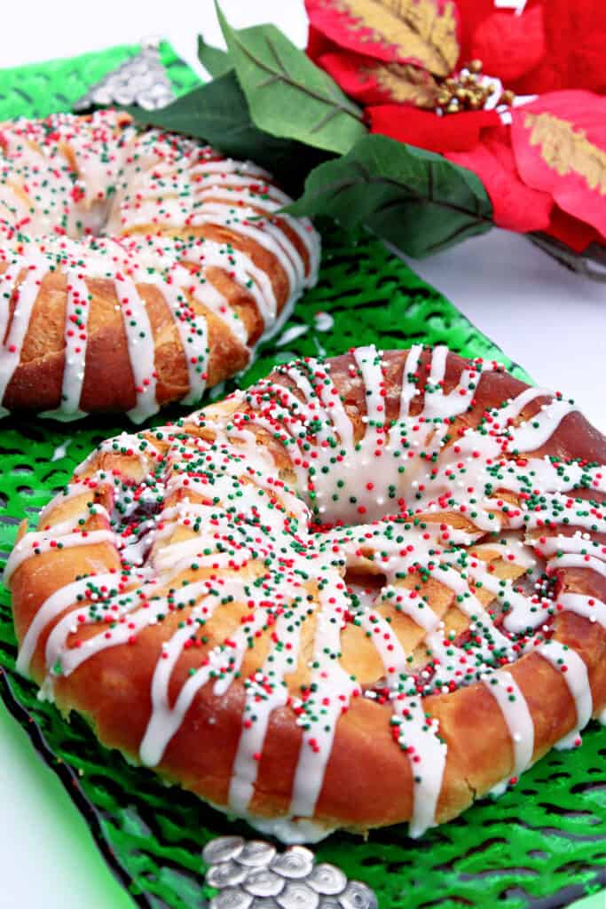 A green glass Christmas platter with a Cranberry Kringle drizzled with icing and sprinkles.