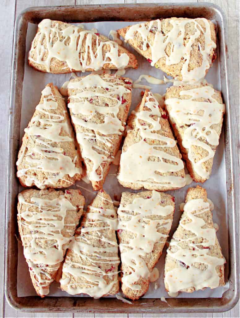 A direct overhead vertical photo of a baking sheet filled with triangle shaped Cranberry Orange Scones with Pistachios.