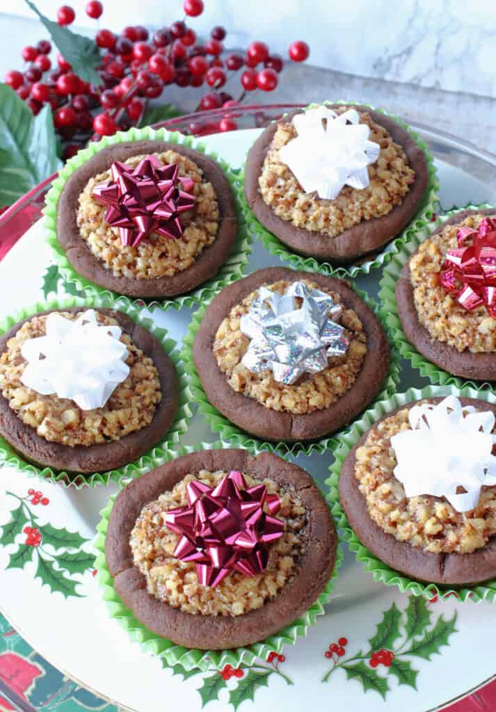 A vertical overhead closeup of a plate filled with Gingerbread Pecan Pie Tarts with Christmas bows on top.