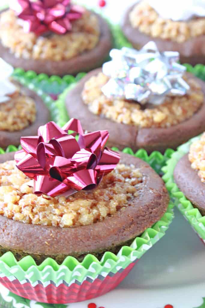 A vertical closeup of Gingerbread Pecan Pie Tarts in muffin cup liners and topped with festive bows.