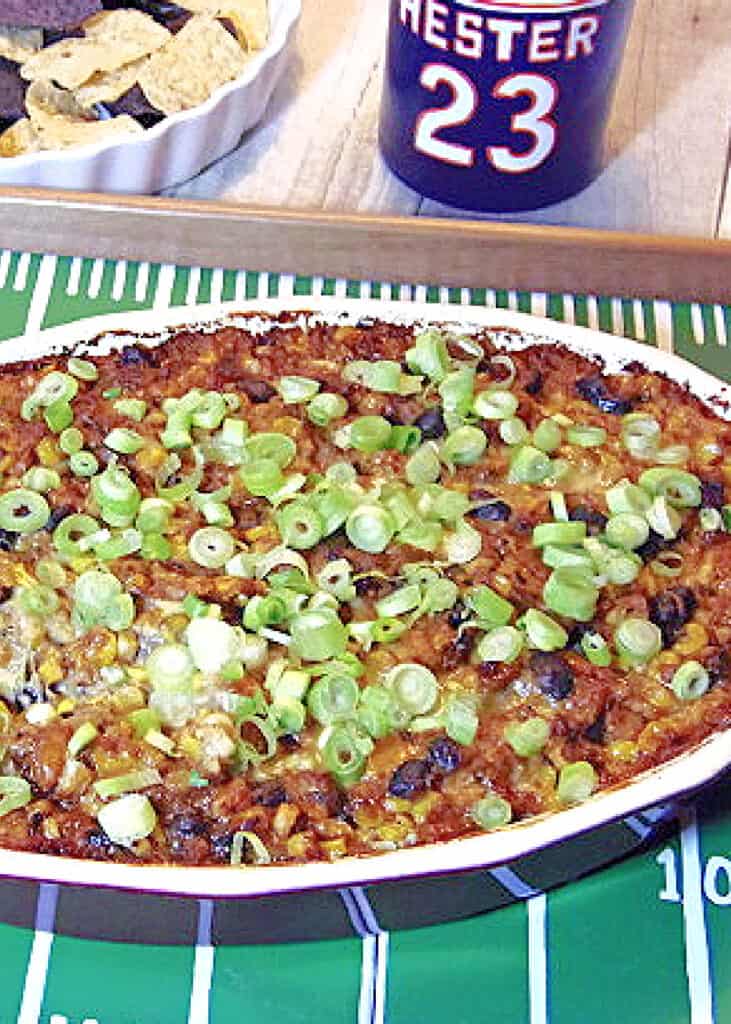 A vertical closeup of some Cheesy Corn and Bean Dip in a baking dish that's been topped with green onion.