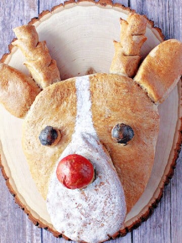 A shaped Rudolph Bread Reindeer on a wooden platter with a painted red nose.