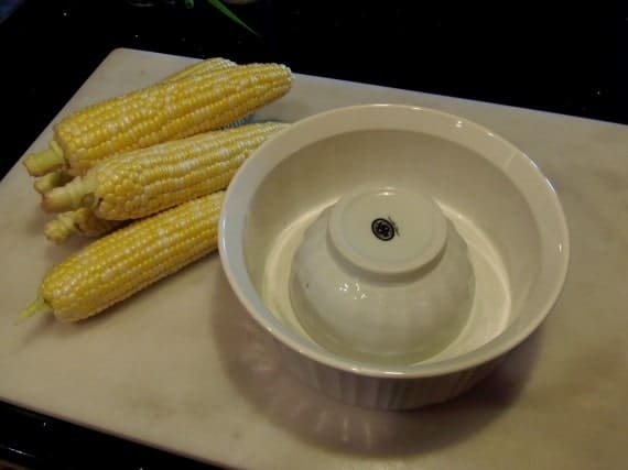 A bowl and some corn on a cutting board.