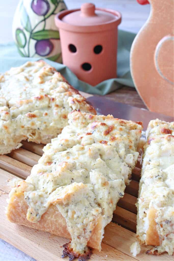 A vertical closeup of a few slices of Chicken Alfredo Garlic Bread Pizza on a wooden bread cutting board.