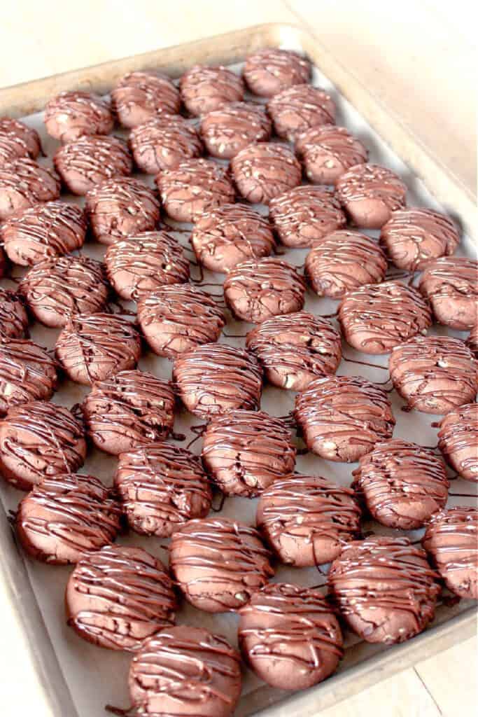 A vertical closeup of a cookie sheet filled with Double Chocolate Creme de Menthe Cookies with a chocolate drizzle on top of each.