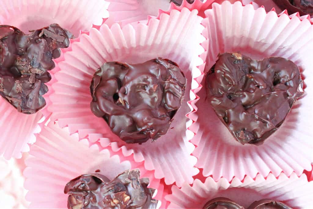 An overhead closeup of heart shaped Chocolate Covered Dried Cherry Clusters in red cupcake paper cups.