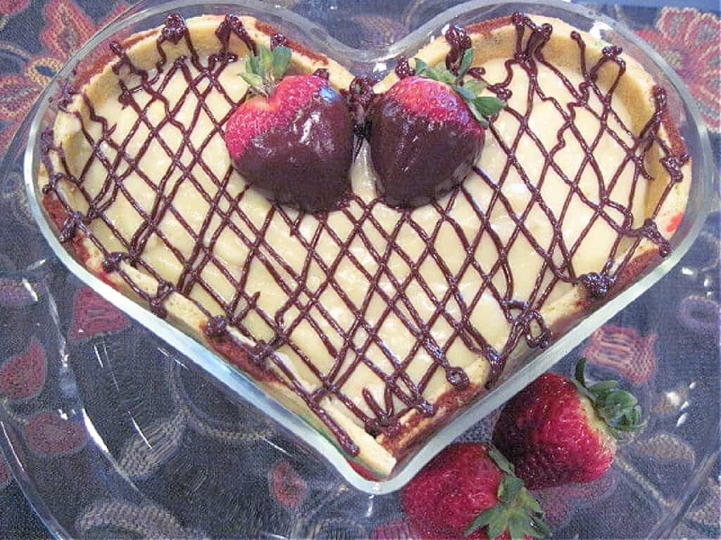 An overhead closeup photo of a Chocolate Covered Strawberry Joconde Entremet in a glass heart trifle dish with chocolate strawberries on top.