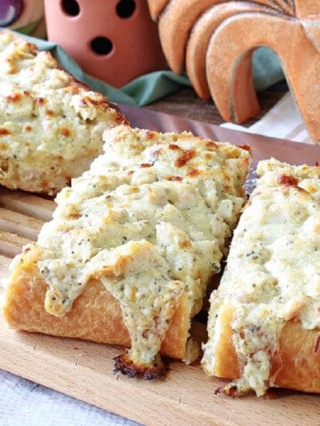 Slices of cheesy Chicken Alfredo Garlic Bread Pizza on a wooden cutting board.