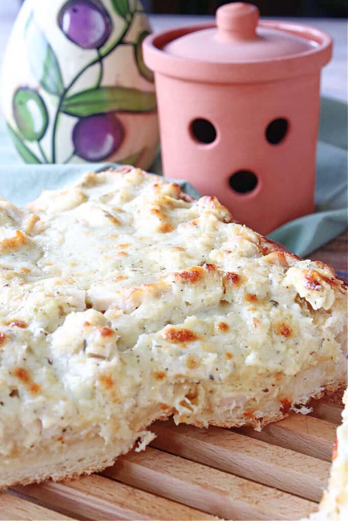 A vertical closeup of a Chicken Alfredo Garlic Bread Pizza cut in half with golden melted cheese on top.