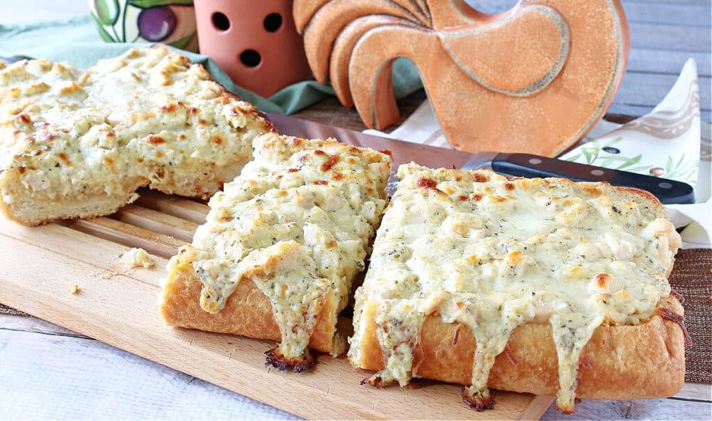 A horizontal photo of a Chicken Alfredo Garlic Bread Pizza cut into slices on a cutting board.