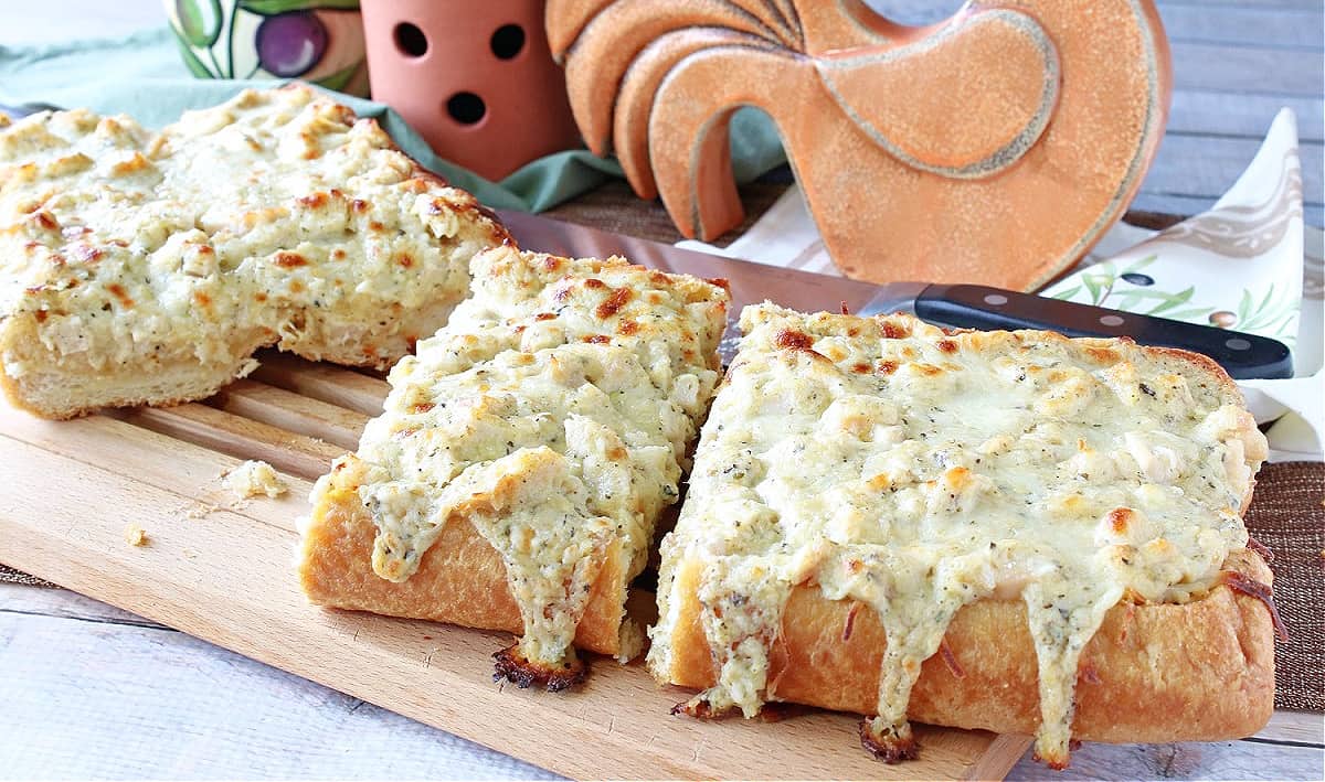 A delicious looking Chicken Alfredo Garlic Bread Pizza on a cutting board with a serrated knife.