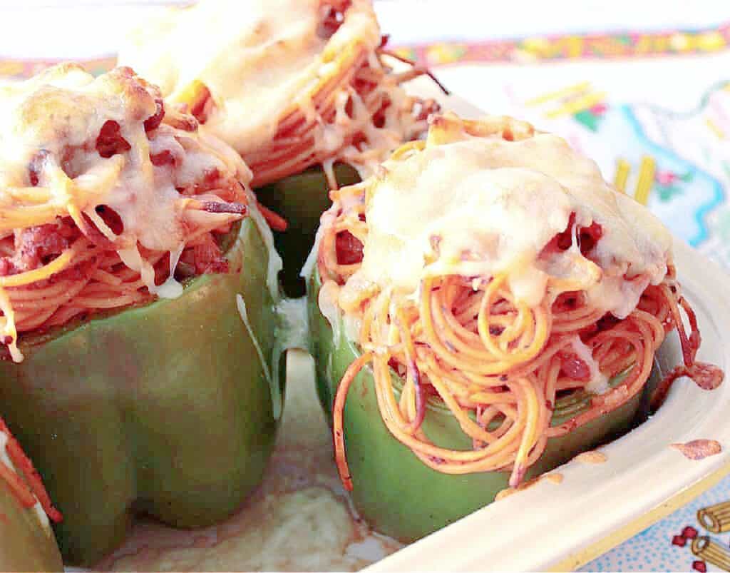 A horizontal closeup of 3 Spaghetti Stuffed Bell Peppers in a casserole dish topped with melted cheese.