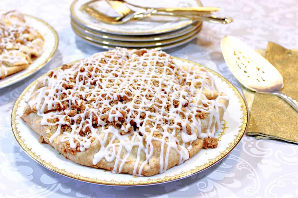 An delicious looking Apple Crumble Crostata on a pretty china plate with a gold rim, and gold napkins in the background.