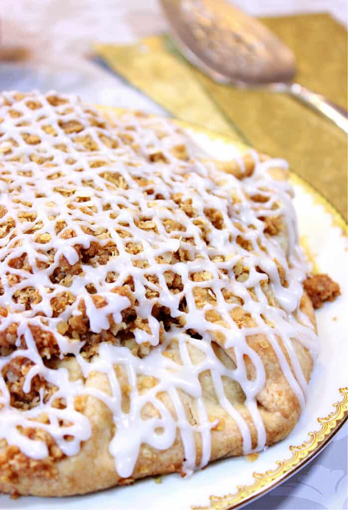 A vertical closeup of an Apple Crumble Crostata with a oat crumble topping and a white icing drizzle.