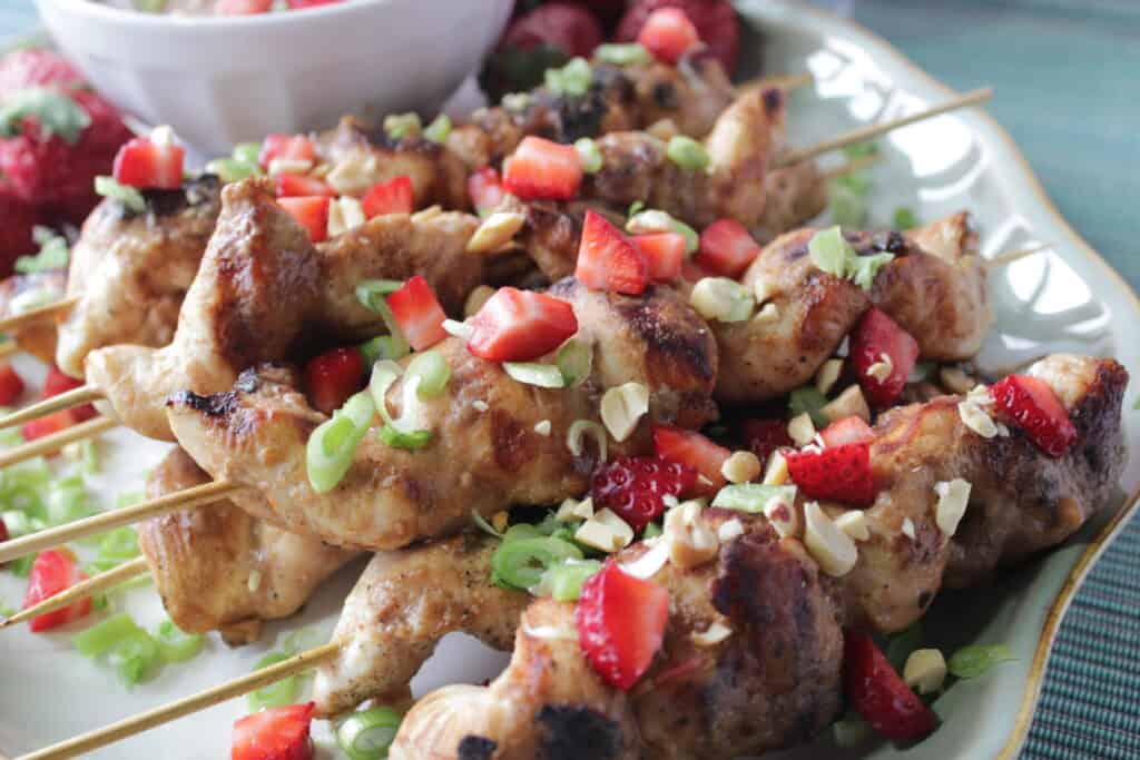 A stack of Chicken with Strawberry Satay Sauce of skewers with chopped peanuts, strawberries, and scallions on top.