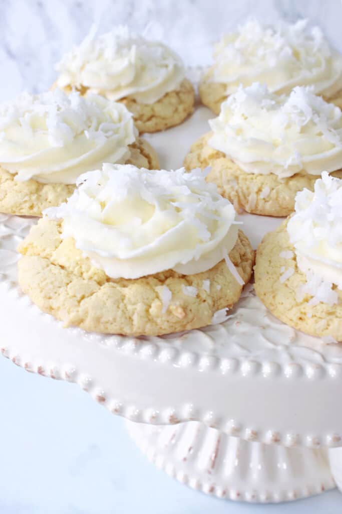 A vertical closeup of Coconut Cake Cookies on a white platter white with buttercream frosting and coconut on top.
